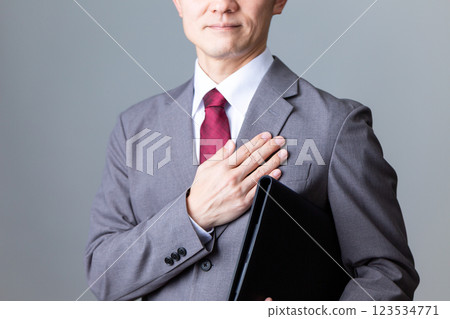 A middle-aged male businessman holding a document and smiling while placing his hand on his chest 123534771
