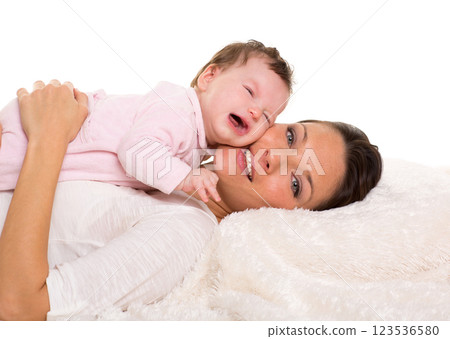 Baby girl crying and mother lying together on white fur 123536580