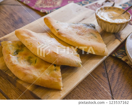 Wooden cutting board featuring warm khachapuri, traditional georgian cheese bread, nestled beside small dipping sauce ramekin, showcasing rich culinary heritage 123537162