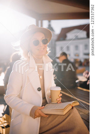Woman enjoys coffee while reading a book in a sunlit outdoor space Woman enjoys coffee while reading a book in a sunlit outdoor space 123537362