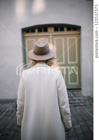 Woman wearing a hat walks towards a vintage door in a serene urban setting Woman wearing a hat walks towards a vintage door in a serene urban setting 123537373