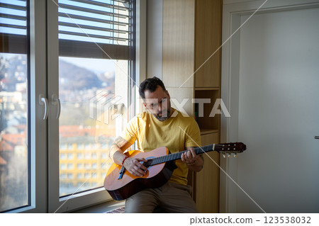 Diabetic man with CGM sensor on arm playing on guitar. 123538032