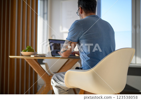 Man with CGM sensor on arm sitting at table and working on laptop. 123538058