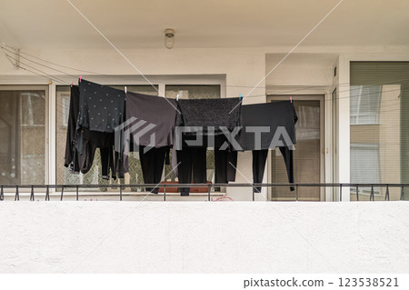 Black clothes hanging on balcony drying line in a residential area. Minimalist monochrome scene of urban laundry routine Black clothes hanging on balcony drying line in a residential area. Minimalist monochrome scene of urban laundry routine 123538521