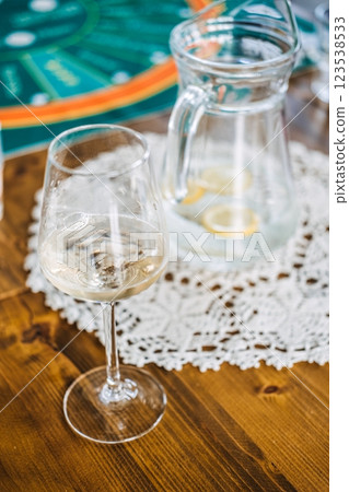 Glass of white wine and pitcher of water with lemon slices on a wooden table, set against a casino-themed game mat Glass of white wine and pitcher of water with lemon slices on a wooden table, set against a casino-themed game mat 123538533