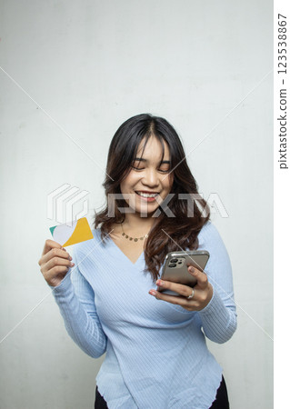 smiling standing woman with mobile phone and shopping card, casual Asian girl blue style, white background studio, advertising shopping mockup 123538867