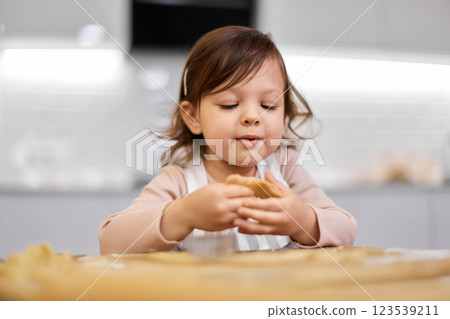 cute happy little child girl cutting gingerbread cookies with a cookie cutter in kitchen. festive gingerbread cookies 123539211