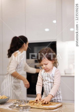 Cute little child girl in apron helping mom bake cookies in modern kitchen 123539226