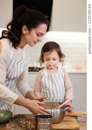 mother and her little child daughter in aprons preparing the dough in the kitchen, bake cookies 123539234
