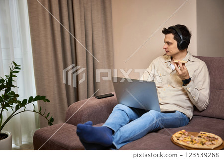 man sitting on sofa and eating pizza while working on laptop 123539268