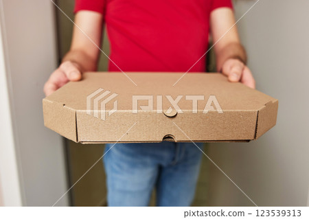 hands of delivery man in red t-shirt giving food order and holding pizza box at home hands of delivery man in red t-shirt giving food order and holding pizza box at home 123539313