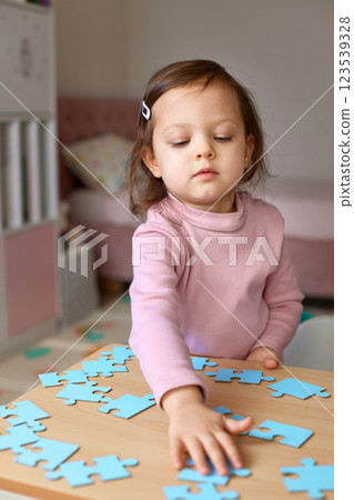 Cute little child girl connecting puzzle pieces on wooden desk in room, children development Cute little child girl connecting puzzle pieces on wooden desk in room, children development 123539328