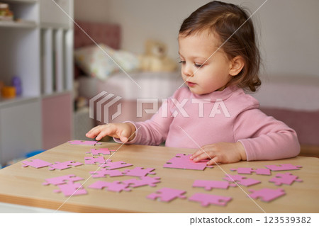 Cute little child girl connecting puzzle pieces on wooden desk in room Cute little child girl connecting puzzle pieces on wooden desk in room 123539382