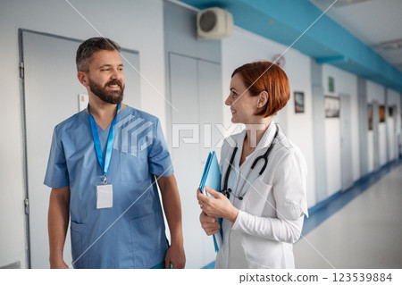 Two doctors walking across hospital hallway, holding medical records in hand. 123539884