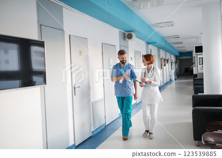 Two doctors walking across hospital hallway, holding medical records in hand. 123539885