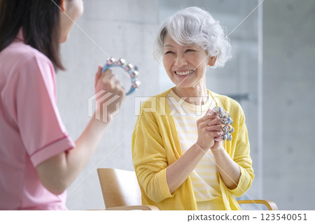 微笑的老年婦女拿著鈴鐺和護理人員音樂練習音樂治療活動圖像 微笑的老年婦女拿著鈴鐺和護理人員音樂練習音樂治療活動圖像 123540051