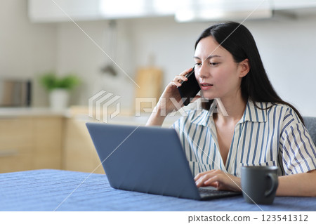 Asian woman checking laptop talking on phone in a kitchen 123541312