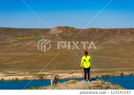 girl in a sports uniform with a dog in the mountains. woman with a husky on background of the steppe girl in a sports uniform with a dog in the mountains. woman with a husky on background of the steppe 123541547