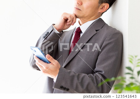 一位中年男性商人一邊看著智慧型手機一邊思考 123541643