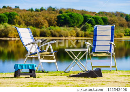 Two empty camp chairs on lake shore Two empty camp chairs on lake shore 123542408