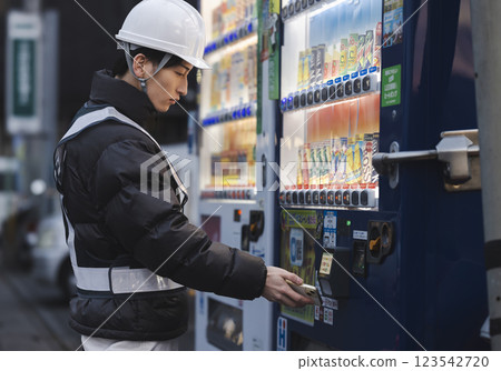 一名穿著工作服的男子正在喝罐裝咖啡 一名穿著工作服的男子正在喝罐裝咖啡 123542720