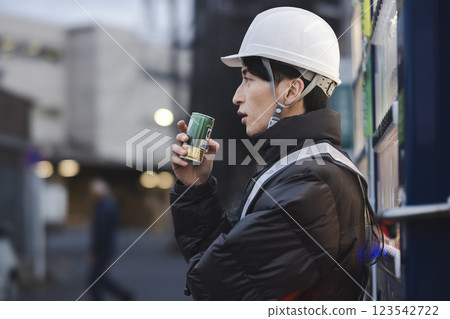 一名穿著工作服的男子正在喝罐裝咖啡 一名穿著工作服的男子正在喝罐裝咖啡 123542722
