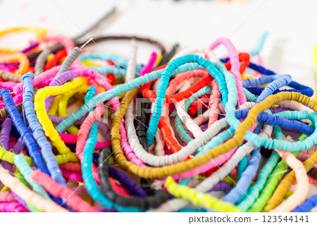 A vibrant collection of clay beads, neatly arranged by color on a white table, ready to inspire young crafters to create their own unique bracelets. 123544141