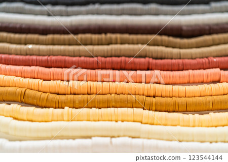 A vibrant collection of clay beads, neatly arranged by color on a white table, ready to inspire young crafters to create their own unique bracelets. A vibrant collection of clay beads, neatly arranged by color on a white table, ready to inspire young crafters to create their own unique bracelets. 123544144