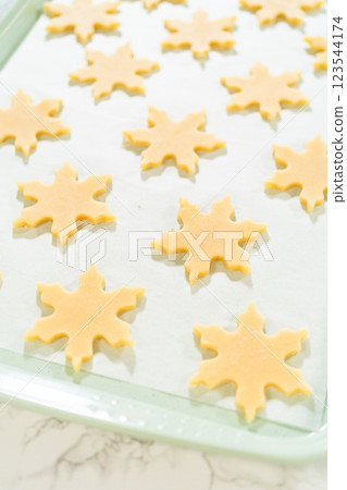 A baking tray filled with star shaped sugar cookie cutouts, placed neatly on parchment paper, viewed from above. A baking tray filled with star shaped sugar cookie cutouts, placed neatly on parchment paper, viewed from above. 123544174