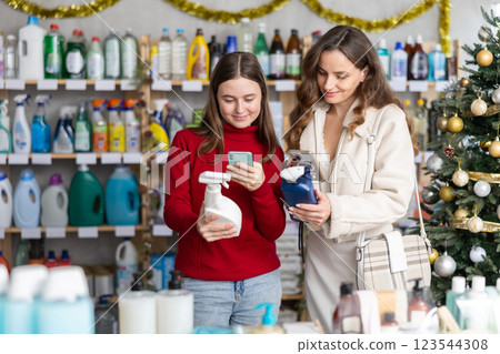 Girl with mother scanning bottle of glass cleaner with smartphone in Christmas store Girl with mother scanning bottle of glass cleaner with smartphone in Christmas store 123544308