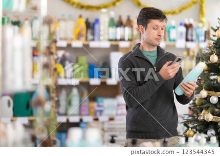 Checking expiration date of shower gel or champoo - male shopper scans QR code on label of shower gel or champoo using smartphone 123544345