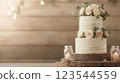 Two tiered rustic wedding cake with white buttercream frosting and pink roses 123544559