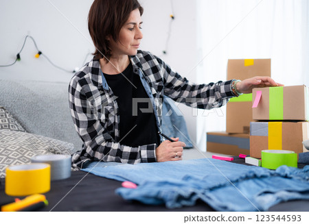 Girl Prepares A Cardboard Box For Shipping With Handmade Clothes 123544593