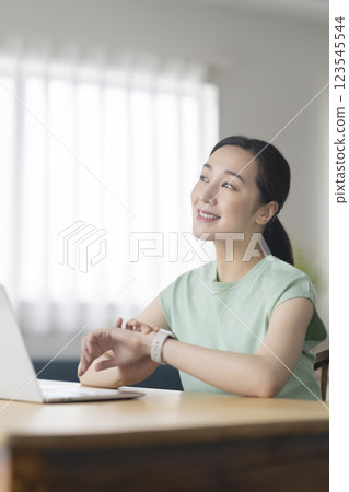 A woman in her 30s touching a smartwatch while working at her desk 123545544