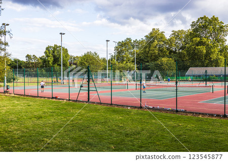 Sunny Outdoor Tennis Courts with Players and in a Public Park 123545877