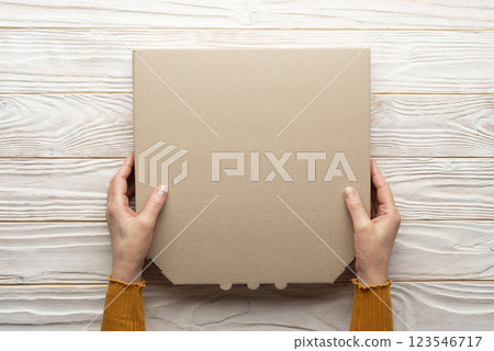 Pizza closed carton box in human caucasian hands on white wooden table flat lay mockup with blank space 123546717