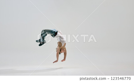 Dancer, dressed casual clothes, arching backwards mid-air, frozen in moment of flight and precision against white background. Dancer, dressed casual clothes, arching backwards mid-air, frozen in moment of flight and precision against white background. 123546770