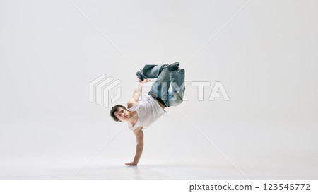 Modern, talented streetdancer, dressed casual attire, in mid-backflip displaying body control in motion against white background. 123546772