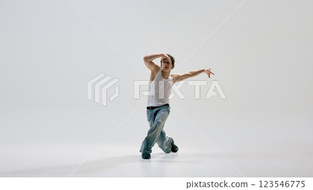 Full length photo of hip-hop dancer, dressed casually, diving forward in mid-motion with controlled technique and focus against white background. 123546775