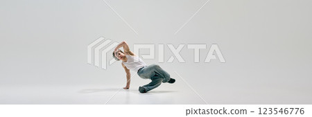 Young dancer, dressed white T-shirt and jeans, flipping mid-air with dynamic energy and expressive movement against white background. 123546776