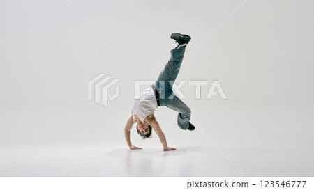 Expressive movement artist stands on hands, pushing physical limits through freestyle dance energy against white background. 123546777