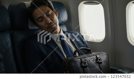 Businessman sleeping on airplane with briefcase on lap 123547032