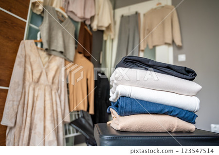 Stacked pile of clothing prepared for resale, donation, or recycling, with wardrobe with outfits in the background. Sustainable fashion choices help reduce waste and support a circular economy 123547514