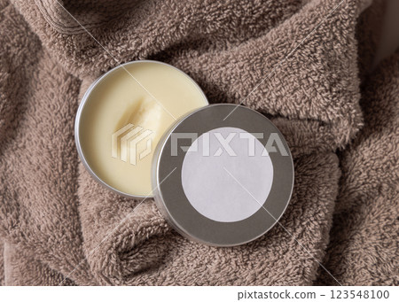Opened body butter jar with blank label on lid on light brown bath towel top view, cosmetic mockup Opened body butter jar with blank label on lid on light brown bath towel top view, cosmetic mockup 123548100