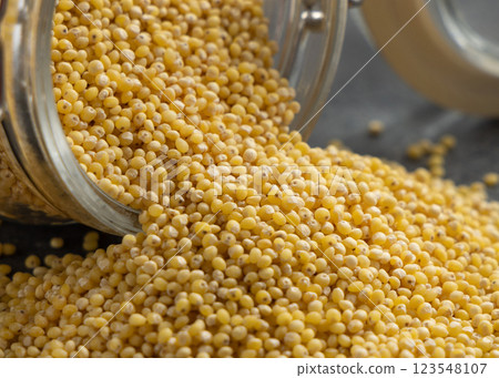 Glass jar of raw yellow pearl hulled millet grain on grey table closeup. Ancient food Glass jar of raw yellow pearl hulled millet grain on grey table closeup. Ancient food 123548107