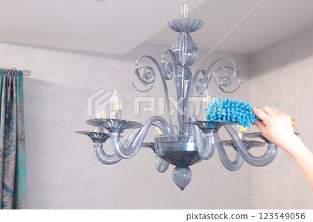 Woman wipe dust on glass chandelier with fluffy broom in living room. Cleanliness and order.  123549056