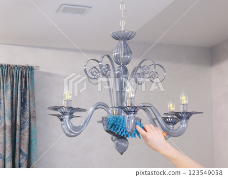 Woman wipe dust on glass chandelier with fluffy broom in living room. Cleanliness and order.  123549058