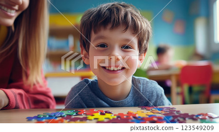 A happy boy at a kindergarten table is engaged with a teacher by collecting jigsaw puzzles A happy boy at a kindergarten table is engaged with a teacher by collecting jigsaw puzzles 123549209