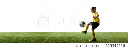 Girl, child in yellow jersey and black short in motion on grassy field, dribbling ball against white studio background 123549326