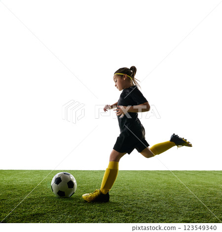 Dynamic image of child wearing black uniform, training on grassy field, controlling ball in motion against white background 123549340